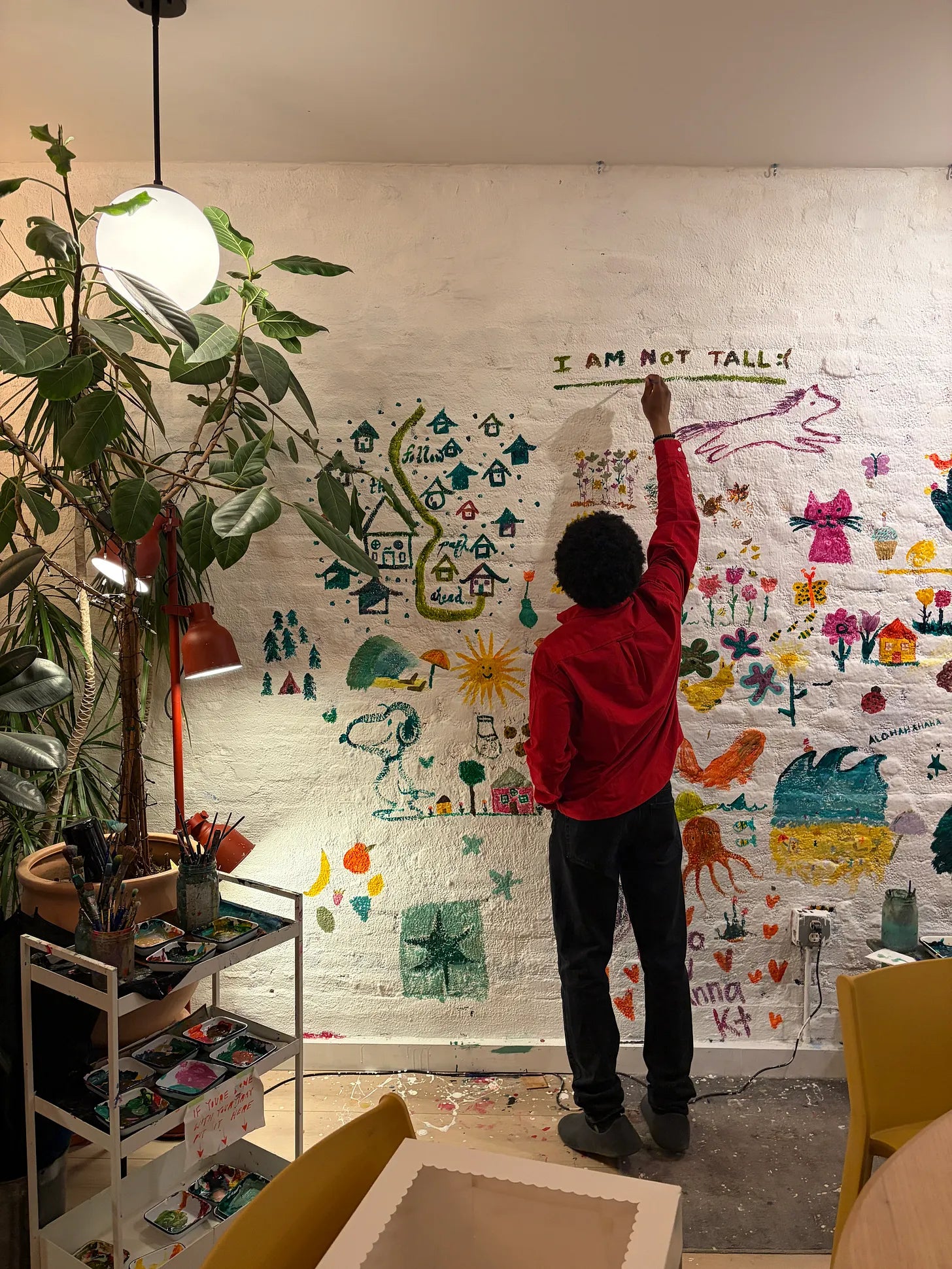 Person writing 'I am not tall' on a colorful illustrated mural wall in an art studio